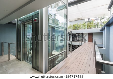 Apartment Interior With Walkway Bridge And Glass Lift Opened.