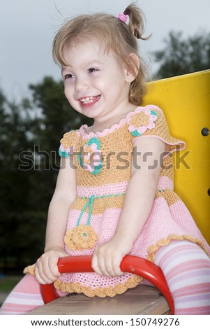 The little girl in knitted dress shakes on swing in park
