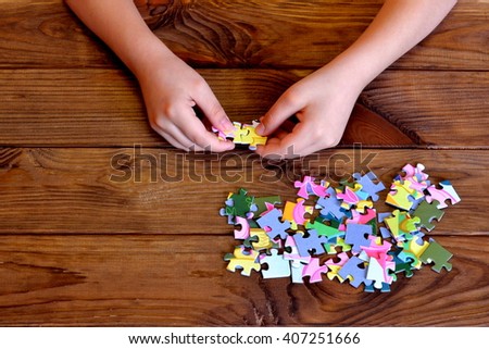Child working on jigsaw puzzle. Child holding a puzzle in hands. Group of jigsaw puzzles on wooden table