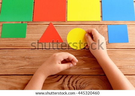 Child holds a yellow cardboard circle in hands and puts on a corresponding color card. Child learns colors. Set of colored cards for kids of preschool age. Idea for learning in kindergarten, at home