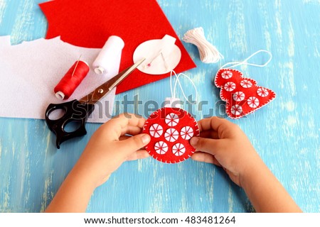 Child holding a Christmas ball in his hands. Child shows Christmas ball. Christmas tree crafts, scissors, thread, needles, felt scraps on a blue background. Sewing concept