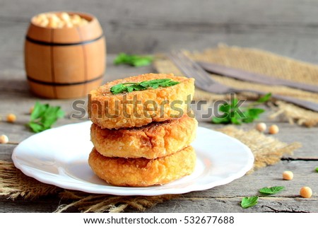 Delicious pea burgers on a plate. Fried vegetarian burgers made from dried peas and decorated with fresh herbs. Decorative wooden barrel, cutlery on a wooden table. Vegetarian meal recipe. Closeup