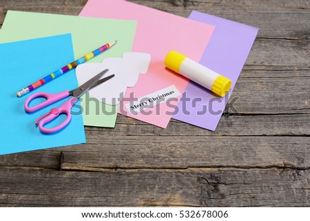 Making a Christmas greeting card. Step. Colored paper set, scissors, pencil, tree template, glue stick, Merry Christmas wishes paper piece on an old wooden table. Simple children Christmas gift idea