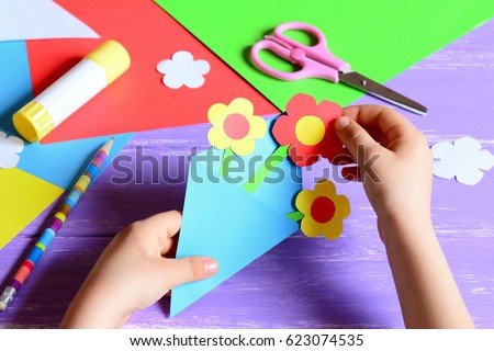 Small child makes paper crafts for mother\'s day or birthday. Small child doing paper flowers for mom. Simple and nice gift idea. Scissors, glue stick, flowers templates, pencil on a wooden table