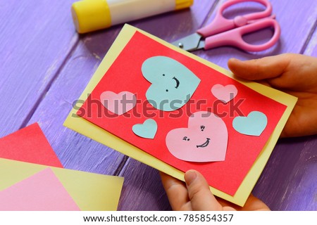 Child is holding a Valentines card in his hands. Child is showing a greeting card. Happy Valentines Day card. Easy paper crafts for kids concept. Closeup