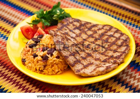 the eal steak with garnish rice with  beans on the yellow plate