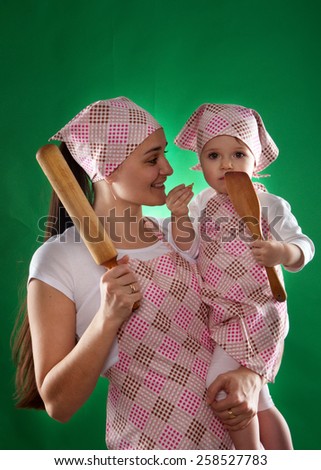 mother and daughter with a scarf and kitchen apron to keep wood rolling pin isolated on the green background