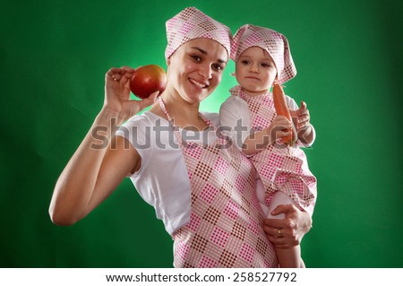 the mother and daughter with a scarf and kitchen apron holding vegetables isolated on the green background.