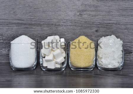 Cube sugar, raw sugar , crystalline sugar and granulation sugar in clear glasses with grey wooden background