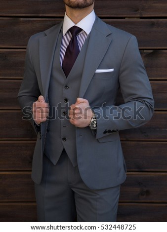 Male model in a three part suit posing in front of a wooden wall