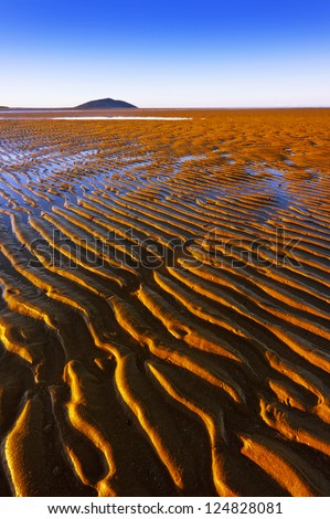 Ripple lines in the sand at low tide disappear into the distance.