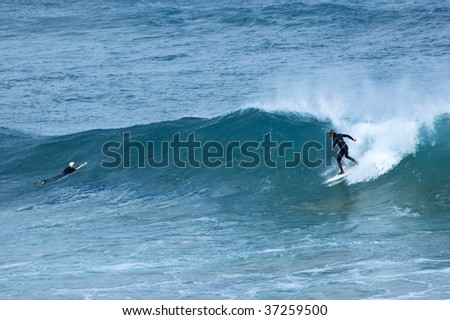 A surfer riding a wave as another surfer paddles over the wave