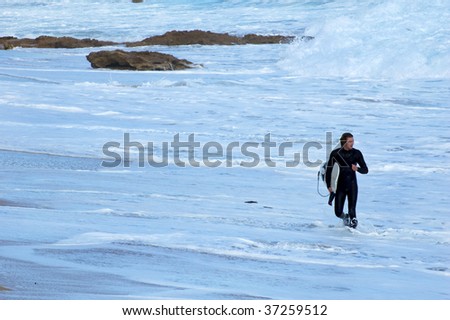 A male surfer after a surf walking through the waves up to the beach