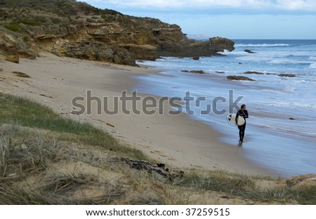 A male surfer walking along the beach looking at the surf