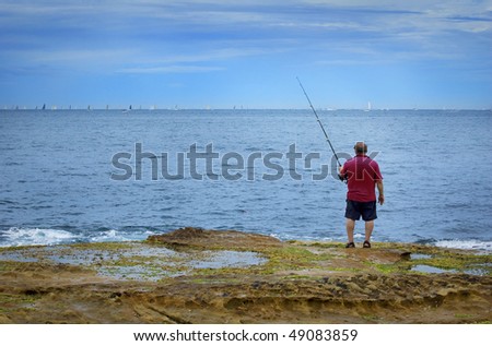 A single man in red shore fishing off rocks in the ocean
