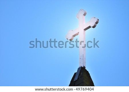Glowing cross atop a steeple against a blue sky