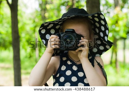 Girl photographer . To look in a lens . Happy childhood . beautiful childhood .  the advanced child . The girl in a hat from the sun. A hat in peas. Settings of a camera