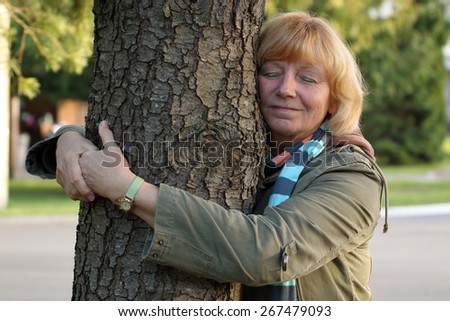 A mature/senior woman hugging a tree outside in the suburbs. Health/peace/nature concept.