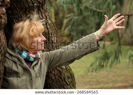 A mature woman reaching out for something from inside of an old tree, outdoors in windy weather.