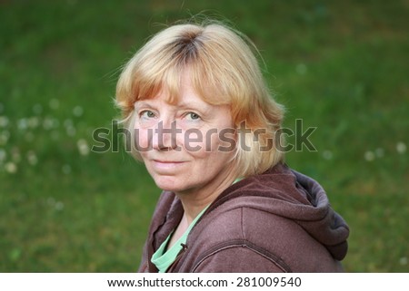 Mature blonde woman smiling outdoors, with green grass background. Health/peace concept.