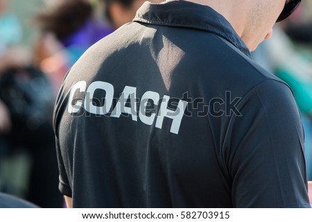 back of a coach\'s black shirt with the white word Coach written on it