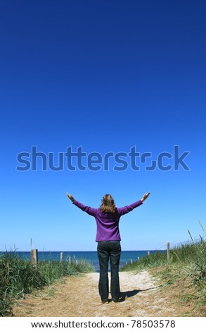 Woman raising hands on a path to the beach