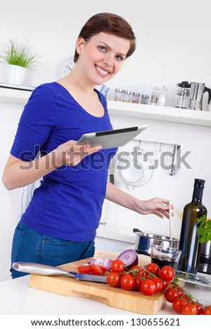 Young woman in her kitchen preparing a pasta dish and  checking the recipe on a tablet pc