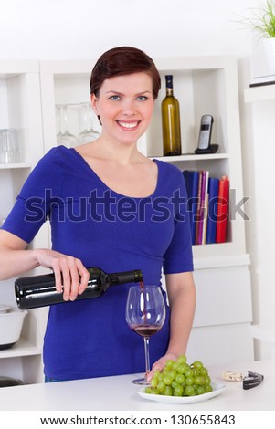 young woman pouring red wine in a glass in her modern kitchen