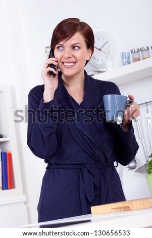 young woman having a cup of tea and talking on the phone in the morning