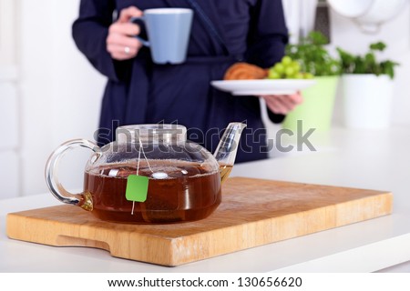 pot of tea and woman holding a healthy breakfast in the background
