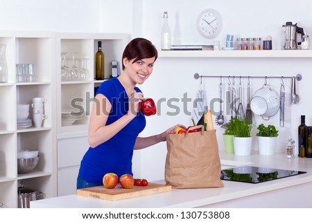 Happy woman unpacking groceries in the kitchen at home