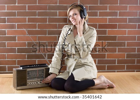 young women in a trenchcoat listens to music of a vintage radio