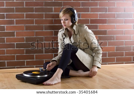 young women in a trenchcoat listens to music of a record player