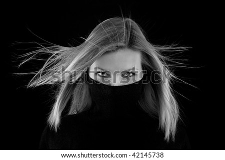 beautiful blonde girl covers her mouth with a black turtleneck on black background (black and white image)