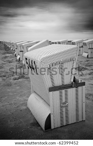Rows of abandoned roofed wicker beach chairs at a beach in black and white