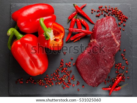 Meat, beef, steak, raw with chili, bell red pepper, sweet pepper, pink pepper, against the background of natural stone