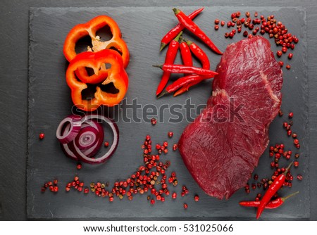 Meat, beef, steak, raw with chili, chopped red bell pepper, sweet pepper, pink pepper, red onion, on a background of natural stone