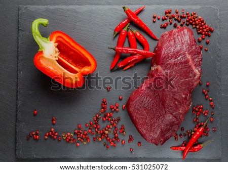 Meat, beef, steak, raw with chili, bell red pepper, sweet pepper, pink, against the background of natural stone.