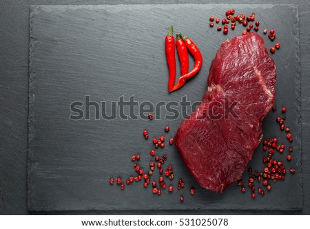 Meat, beef, steak, raw with chili pepper, pink pepper, against the background of natural stone