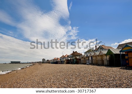 Pebble beach with a row of small huts, with a pier stretching out to sea in the background. Taken at Herne Bay, Kent, England.