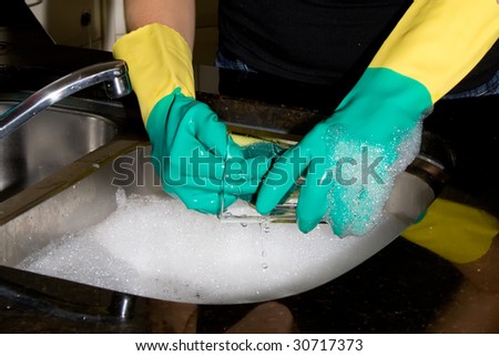 Woman washing up a glass wearing rubber gloves