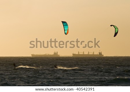 View of a pair of kitesurfers just before sunset, with large sea container ships in the far background