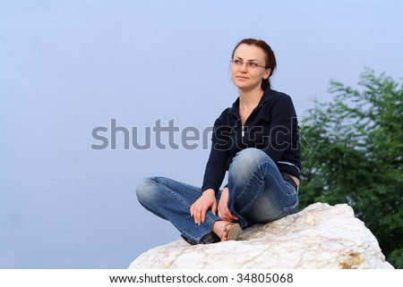 The girl looks afar having a rest sitting on a marble rock
