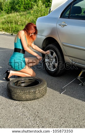 Pretty girl is trying to change a tire on a road