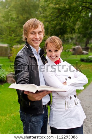 Two students with open book in the park