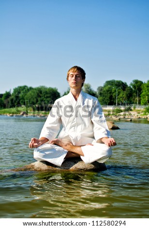 Man in kimono meditating on the rock in the sea