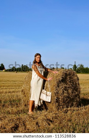 girl in a rural clothing with bag standing near haystack,