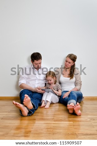 Happy family sitting on the floor against the wall and using tablet computer