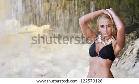 Young girl in black bikini standing under waterfall