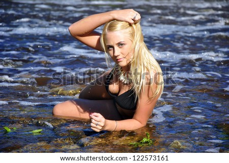 Young girl in black bikini lying on river shore